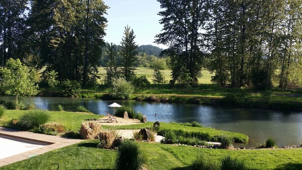 A serene riverside landscape with a grassy area, a paved path, and a small seating area with a white umbrella. - Exceptional retreat near University of Oregon Athletics. Casa del Roots (Eugene)