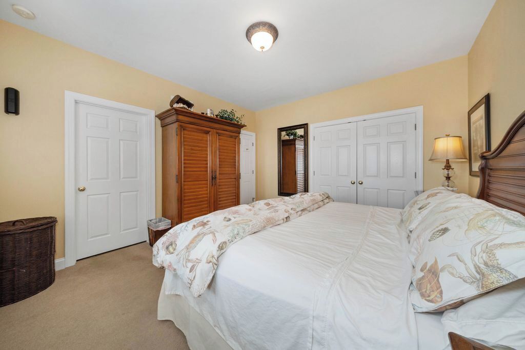 Un dormitorio con cama, dos puertas, un armario de madera, una lámpara y un cubo de basura.