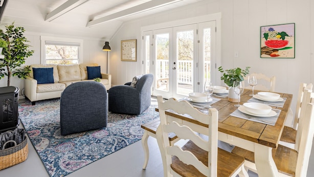 A cozy living room with a sofa, two armchairs, a dining table set for four, and a large window with a view of the outdoors.