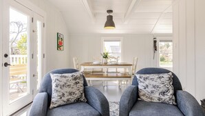 A room with two grey armchairs, a wooden dining table, and a hanging pendant light.