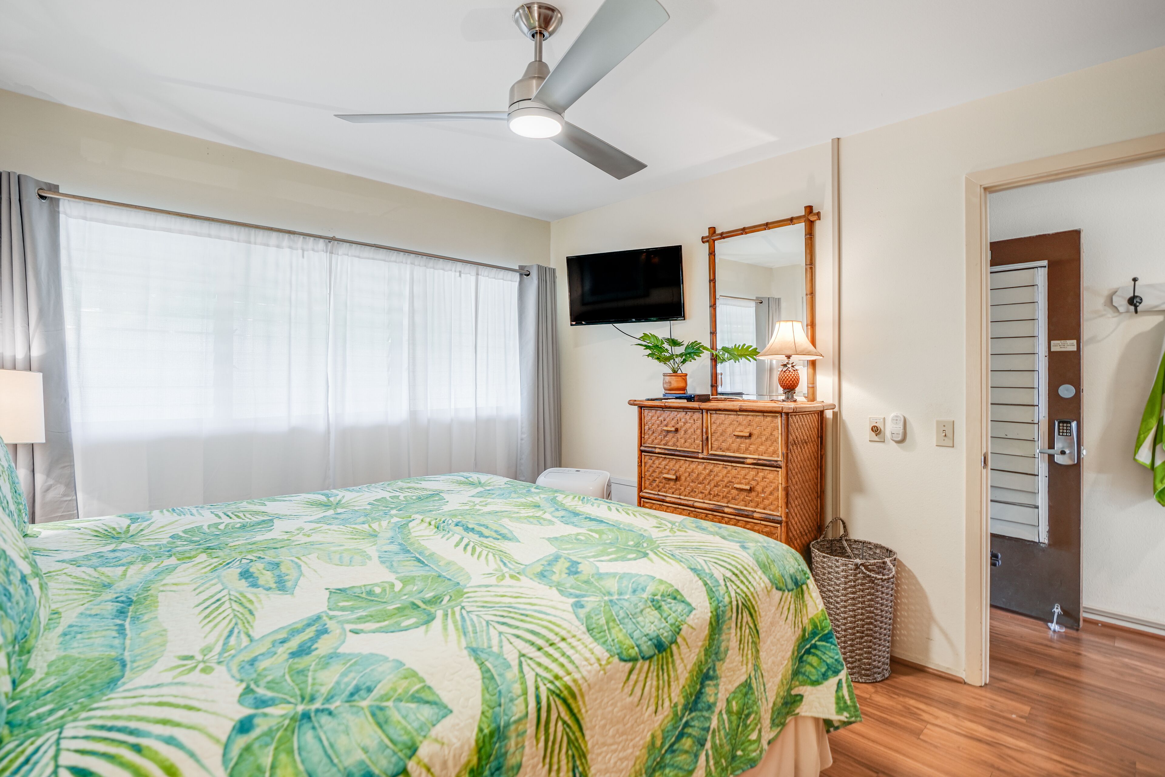 Une chambre à coucher avec un lit, un ventilateur de plafond, une télévision, une commode et une porte menant à la salle de bain.