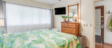 Une chambre à coucher avec un lit, un ventilateur de plafond, une télévision, une commode et une porte menant à la salle de bain.