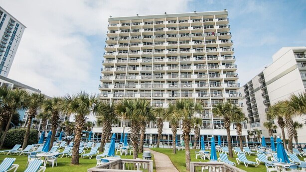 A high-rise hotel with multiple balconies, a pool area with sun loungers and umbrellas, and a pathway leading to the pool. - Direct Oceanfront, In the middle of happening area (Myrtle Beach)