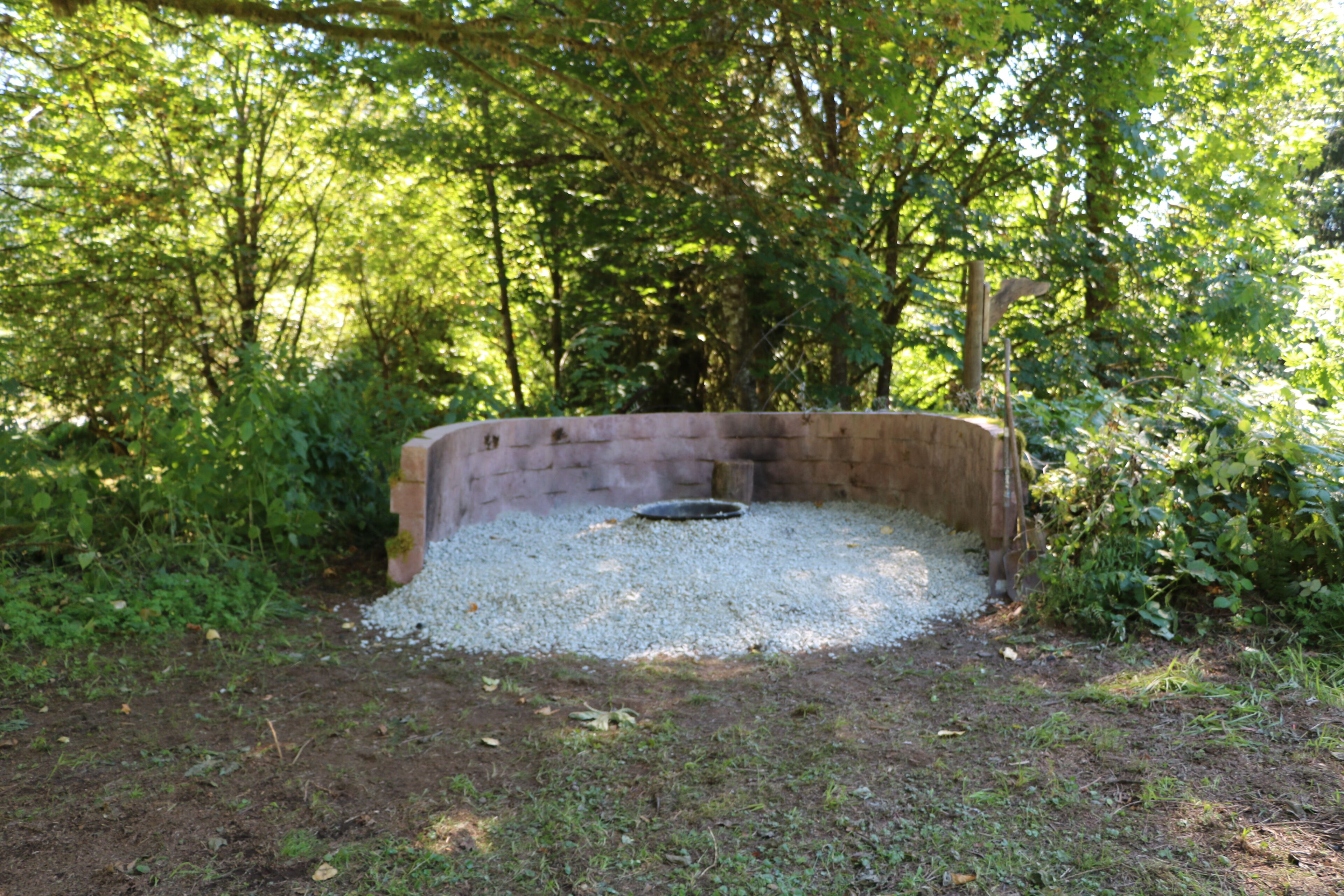 A circular stone structure surrounded by gravel, set in a wooded area.