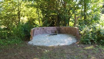 A circular stone structure surrounded by gravel, set in a wooded area.