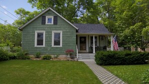 Ett grönt hus med en veranda, en liten trädgård och en amerikansk flagga.