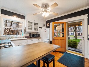 Une cuisine avec des armoires blanches, un plan de travail en bois, un ventilateur de plafond et une vue sur l’extérieur.