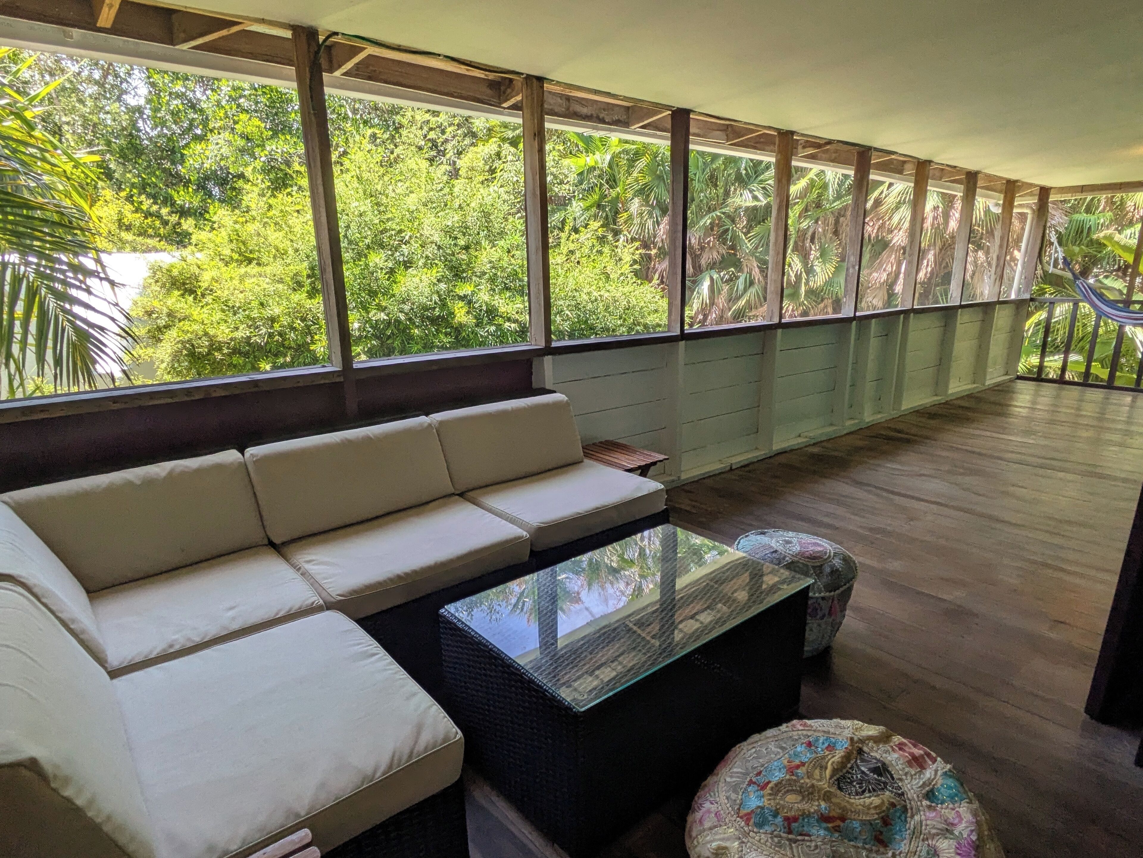 Ein Zimmer mit einer Couch, einem Glastisch und Blick auf üppiges Grün durch große Fenster.