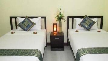 Habitación de hotel con dos camas, cada una con una almohada y una mesita con lámpara. Dos cuadros enmarcados adornan la pared sobre las camas.