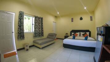A room with a bed, a sofa, a small table, a refrigerator, and a window with curtains.