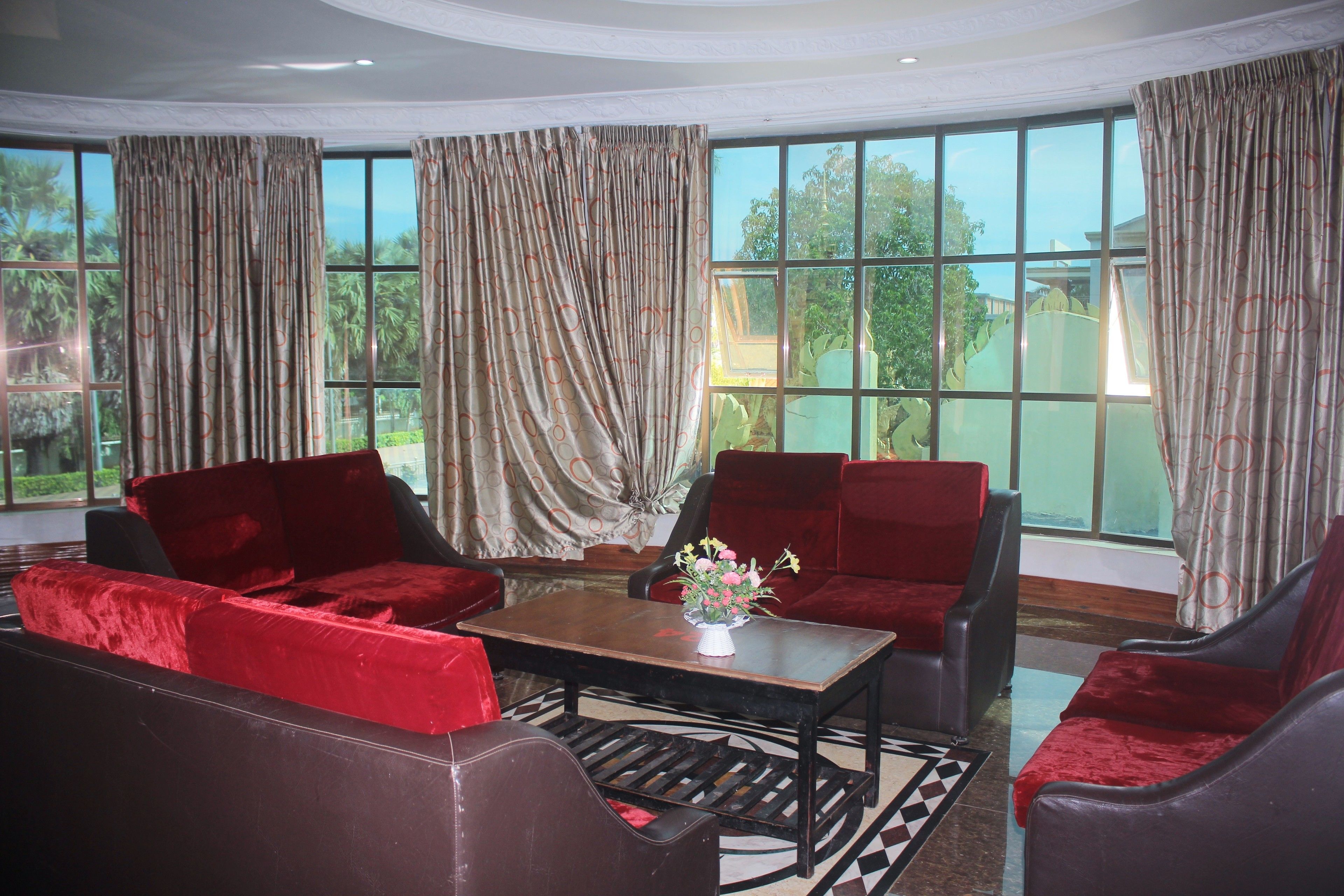 Una habitación con ventanas amplias, muebles tapizados en rojo y una mesa de centro de madera con un jarrón de flores.