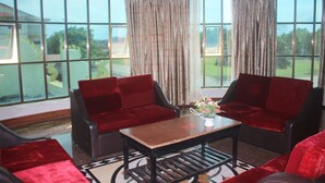 A room with a large window, red upholstered chairs, a wooden coffee table, and a vase with flowers. - 7 Makara Hotel (Kampong Cham)