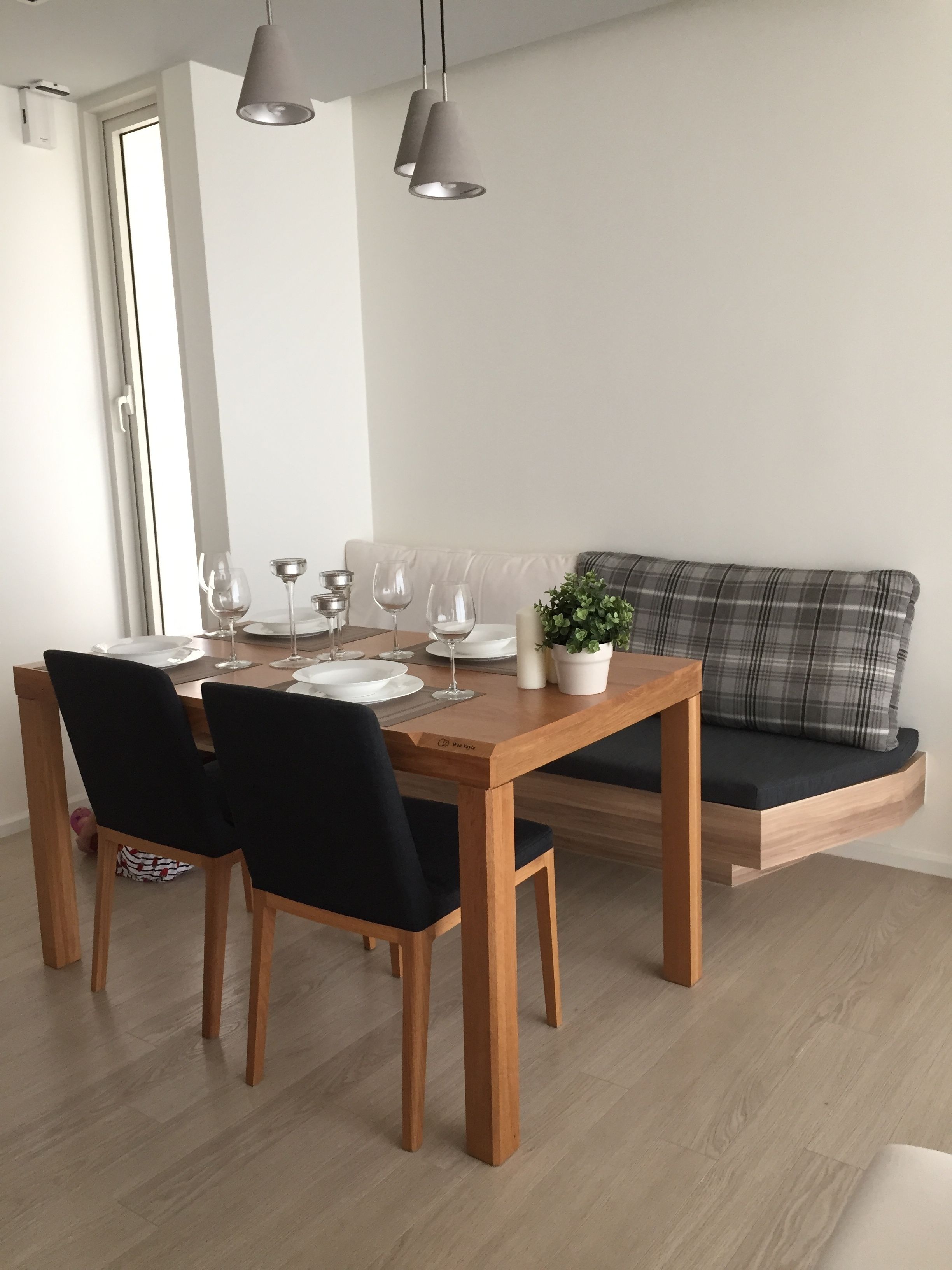 A modern dining area with a wooden table set for four, black chairs, and a grey sofa.