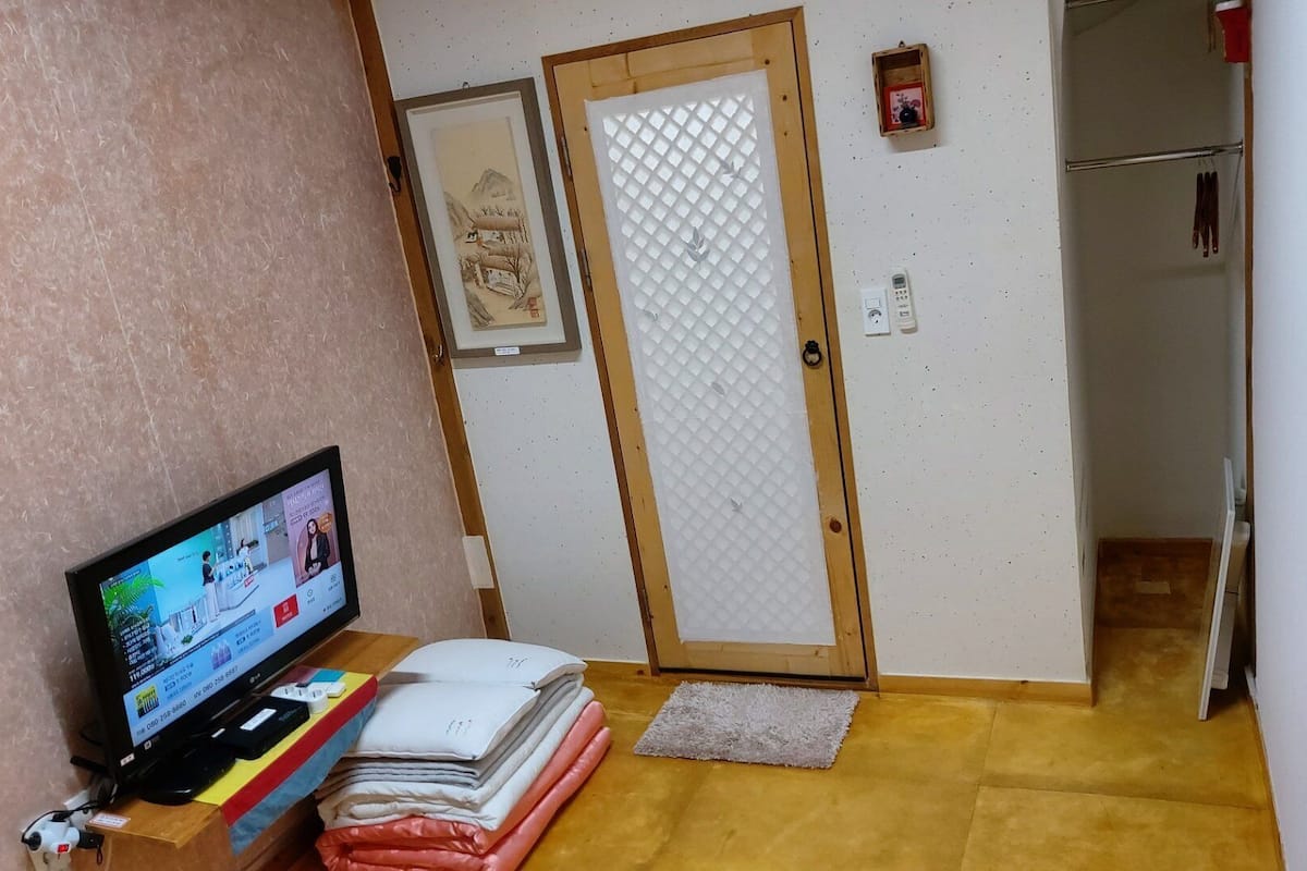 A room with a television displaying a shopping website, a wooden door with a frosted glass panel, and a small shelf with folded towels.