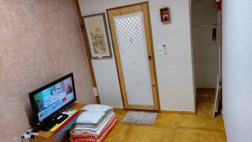 A room with a television displaying a shopping website, a wooden door with a frosted glass panel, and a small shelf with folded towels.