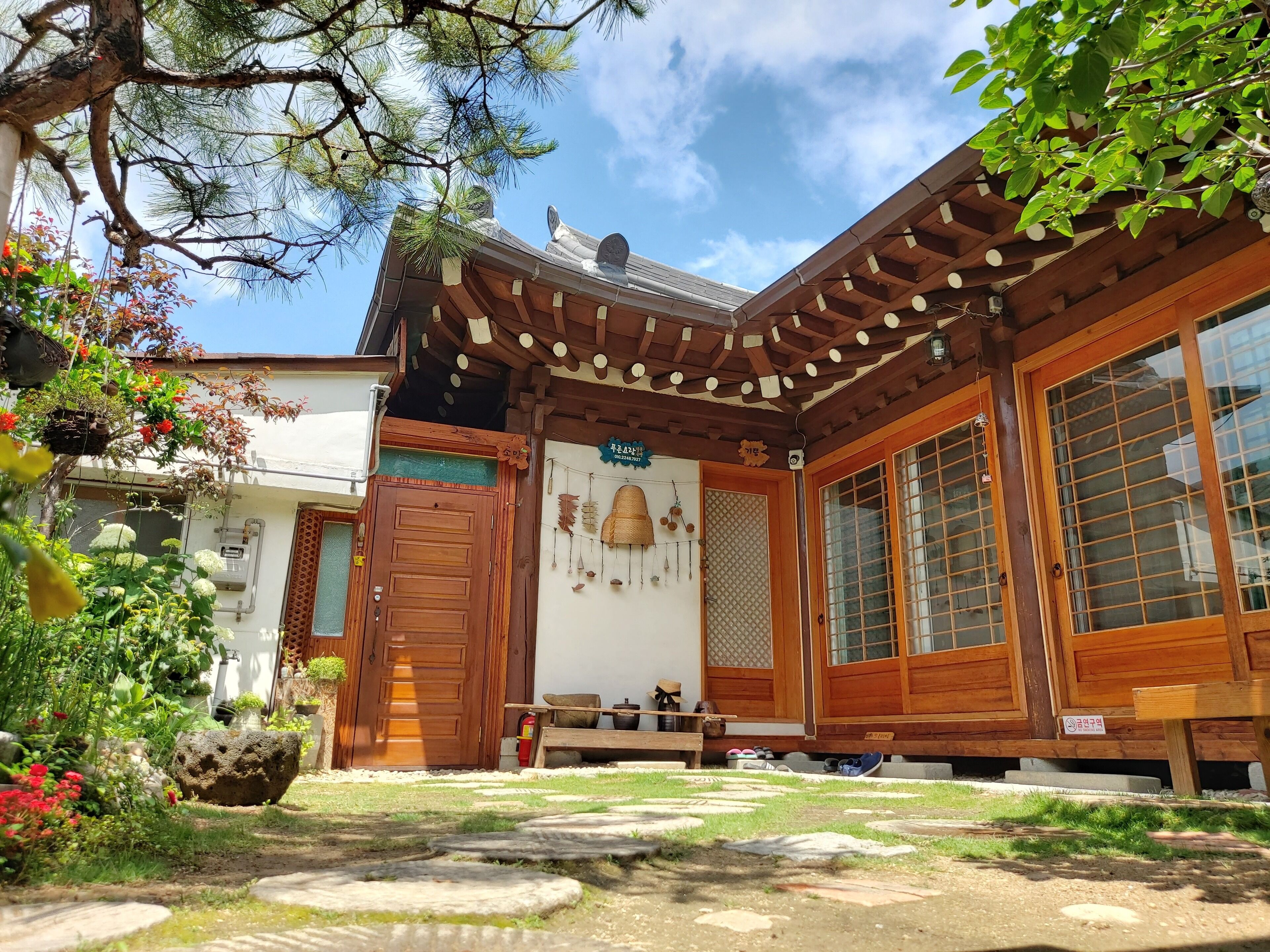 Il s'agit d'un bâtiment de style japonais traditionnel, avec une façade en bois, de grandes portes coulissantes et un petit jardin agrémenté de pierres plates et de plantes.