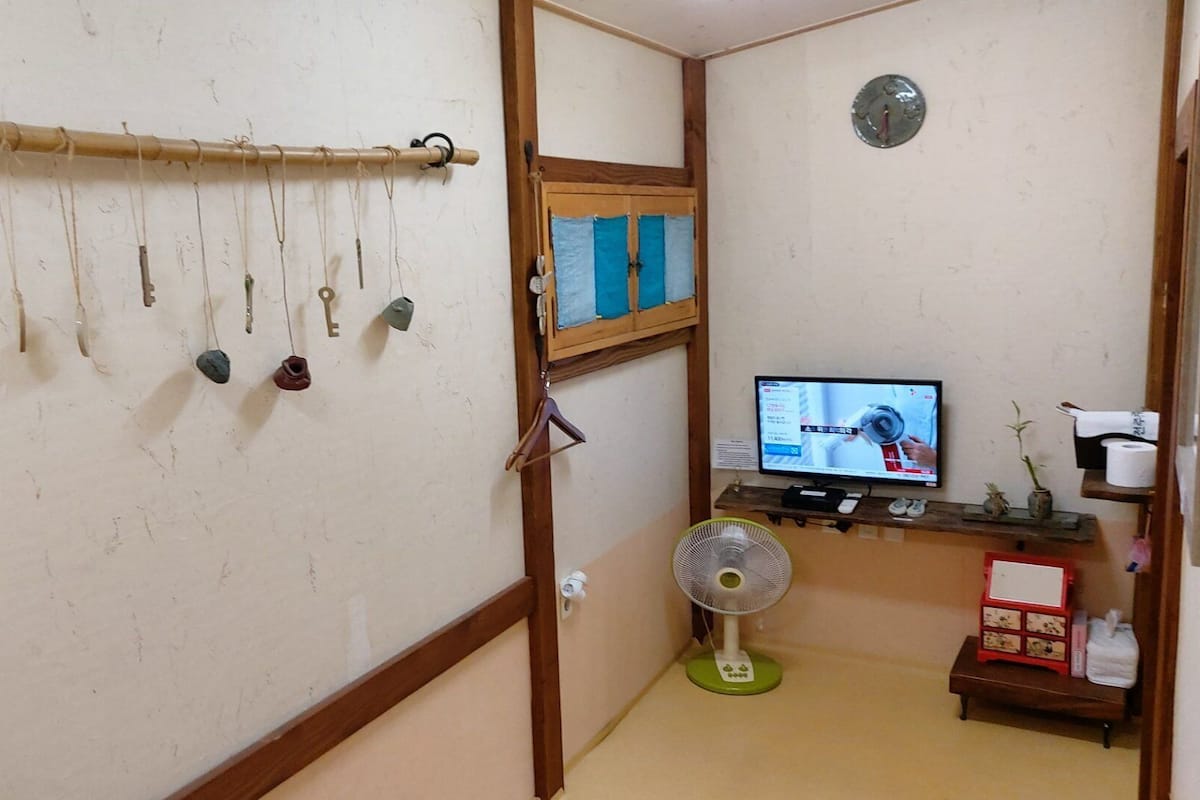 A room with a bamboo curtain rod, a television, a fan, and a small shelf with items.