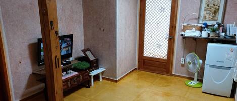 A compact living space with a wooden door, a small refrigerator, a television, and a fan.