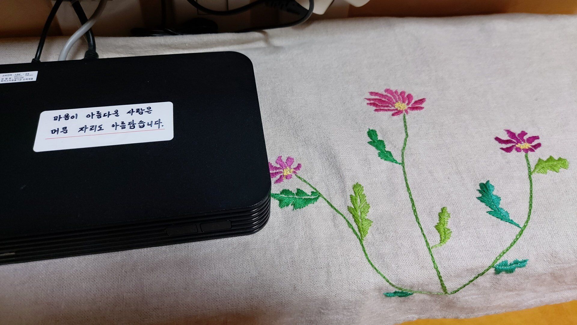 A black electronic device with a label in a foreign language, placed on a fabric with embroidered flowers.