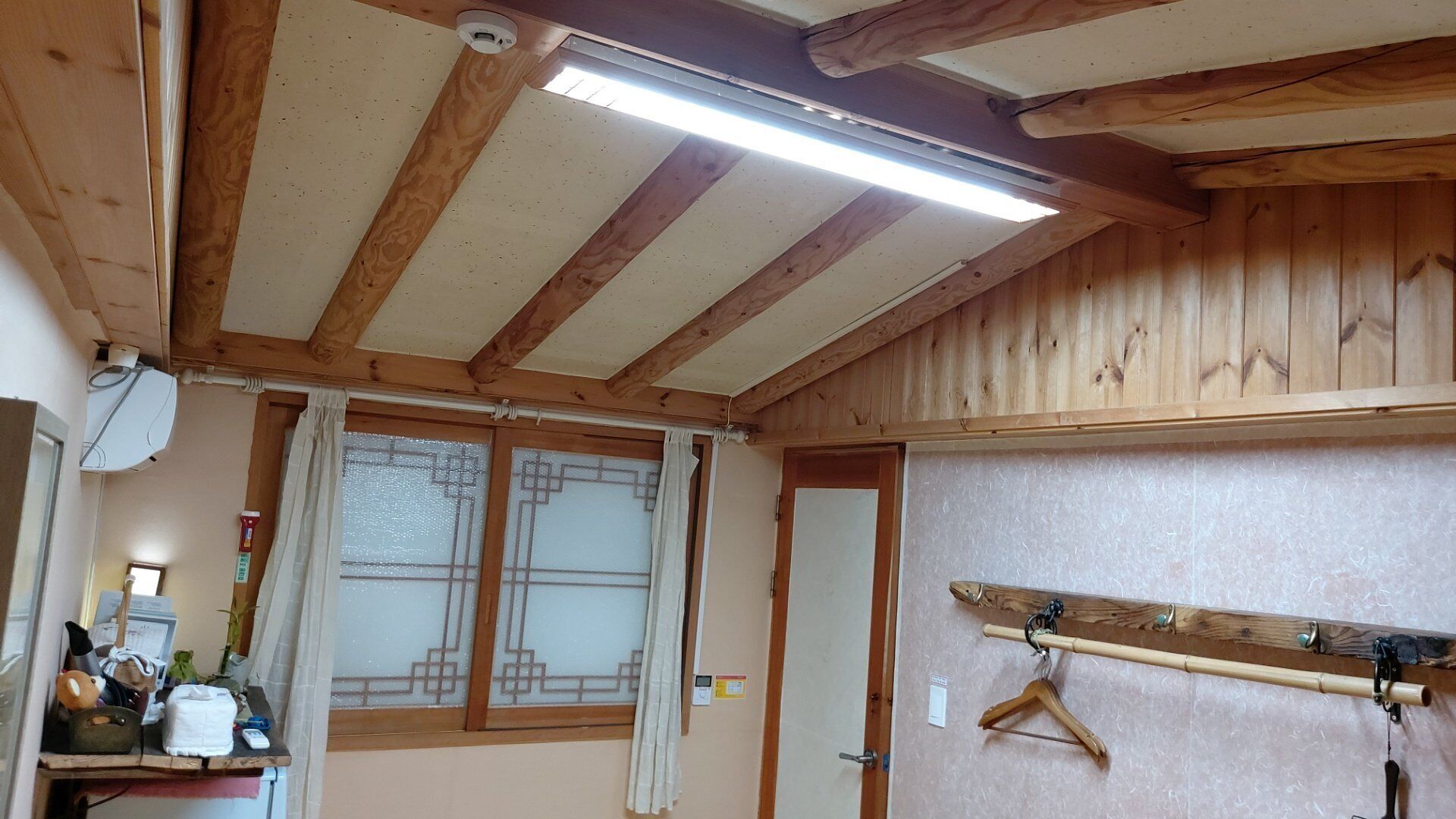 A room with wooden beams, a window with frosted glass, a wall-mounted coat rack, and a door.