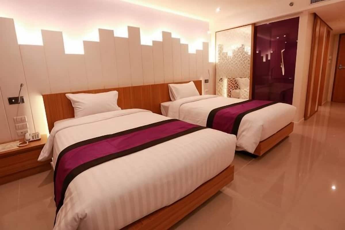 Une chambre d’hôtel avec deux lits, une table de chevet, une lampe fixée au mur et un miroir.