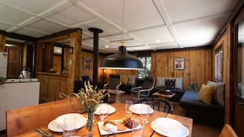 A wooden interior with a dining table set for four, a sofa, and a large pendant light.