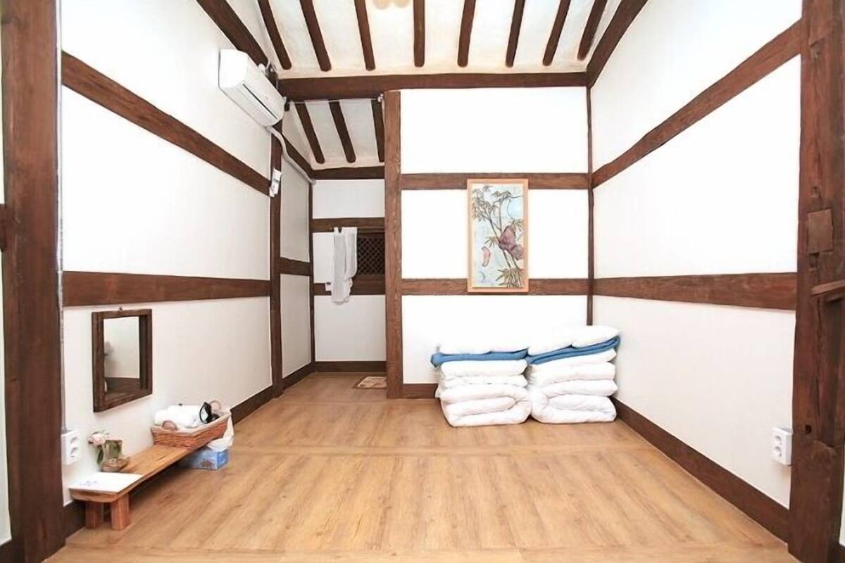 Een traditionele Japanse kamer met tatami vloeren, een houten balkenplafond, een spiegel, een klein plankje met toiletartikelen en een stapel handdoeken.
