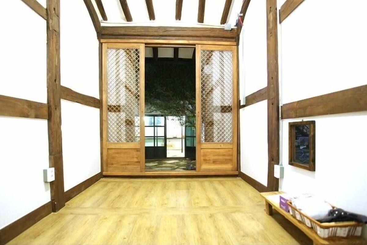 Een kamer met een houten vloer, een schuifdeur met uitzicht en een klein bankje met spullen erop.