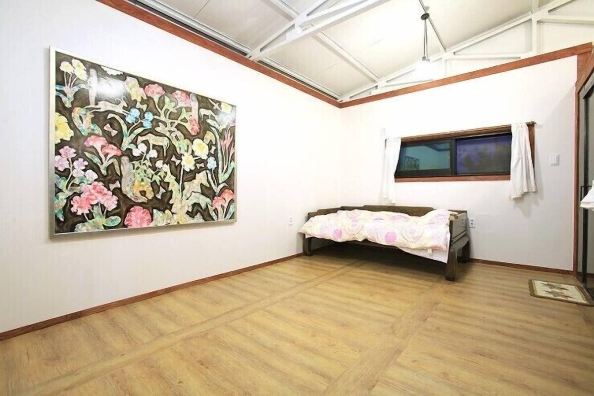 Een kamer met een groot bloemschilderij aan de muur, een bed met een bloemenbedekking en een raam met gordijnen.
