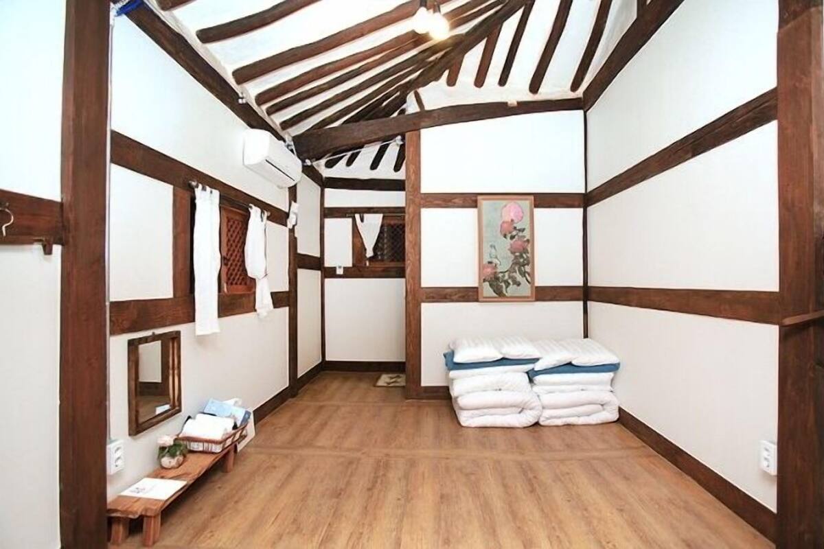 Een kamer met zichtbare houten balken, een houten bankje, een spiegel en een schilderij aan de muur.