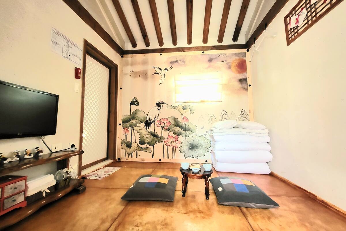 Une pièce avec un plafond en bois, un téléviseur fixé au mur, un tableau représentant des oiseaux et des fleurs, une petite table avec des tasses et une pile de serviettes.