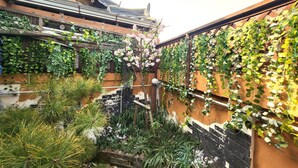 A traditional courtyard with a wooden staircase, lush greenery, and a tiled roof. - Sori poonggyung (Jeonju)