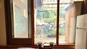 A room with a sliding glass door leading to a garden, a wooden table with bowls and a plate, and two cushions on the floor. - Sori poonggyung (Jeonju)