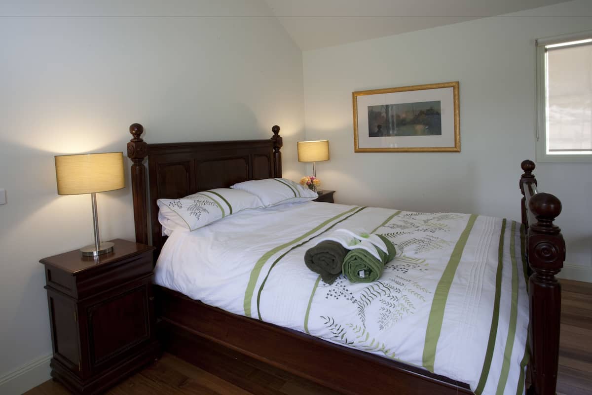 A neatly made bed with a wooden headboard, two bedside tables with lamps, a framed picture on the wall, and a window with blinds.