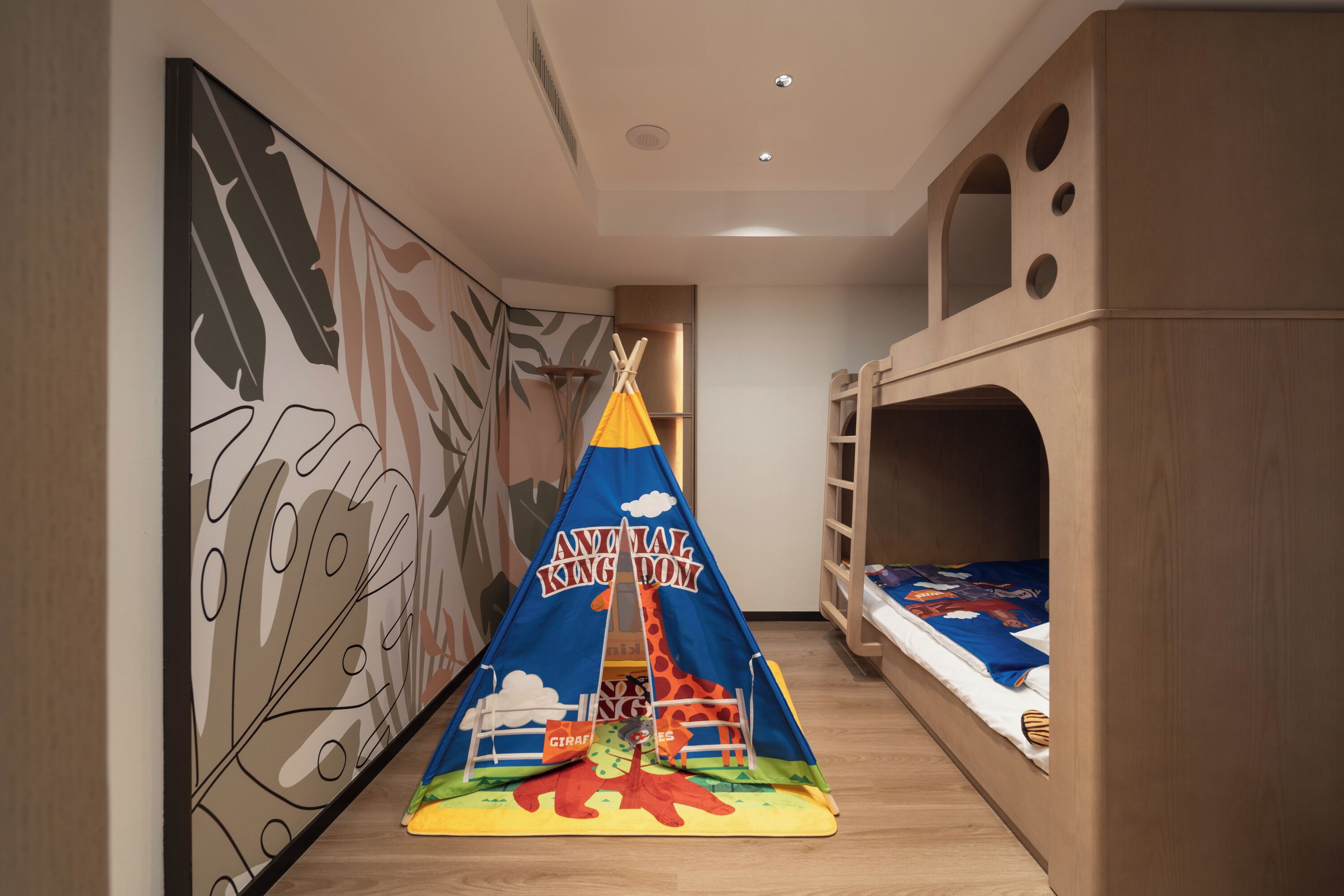 Un área de juegos infantiles con una carpa identificada como "Animal Kingdom", camas literas y una pared decorada con diseños de hojas.