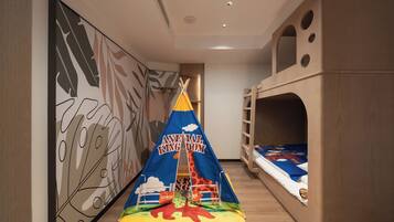 Un área de juegos infantiles con una carpa identificada como "Animal Kingdom", camas literas y una pared decorada con diseños de hojas.