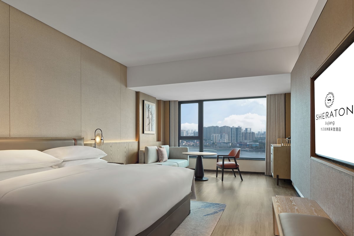 A modern hotel room with a large bed, a desk, and a view of the city skyline.
