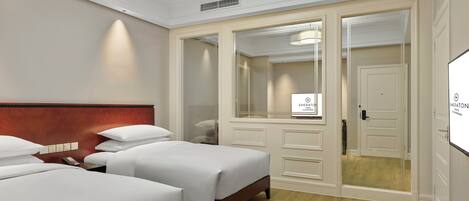 A hotel room with two single beds, a wooden headboard, a large mirror, a wardrobe, and a ceiling light.