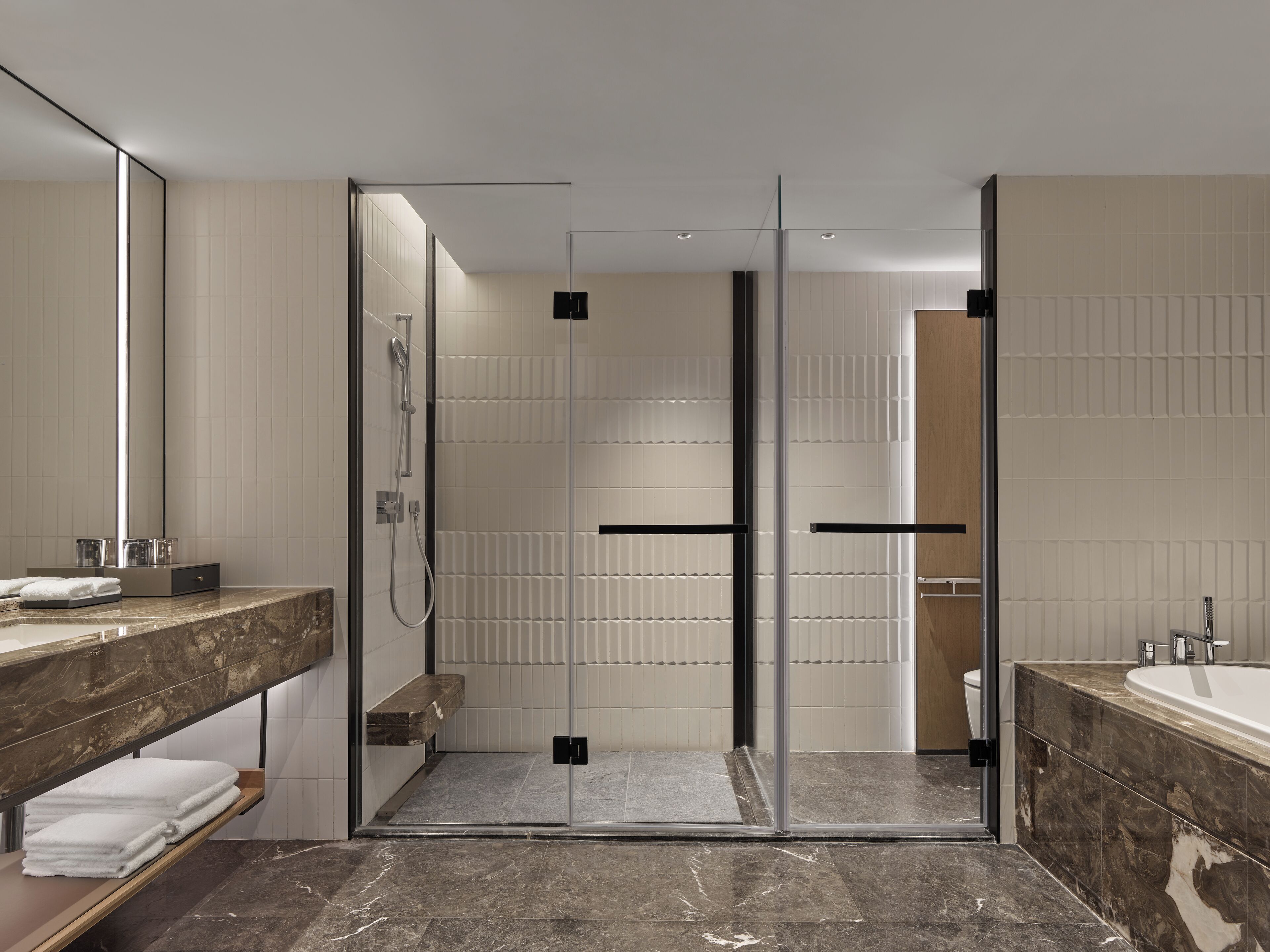 A modern bathroom with a glass-enclosed shower, marble countertops, and a large mirror.