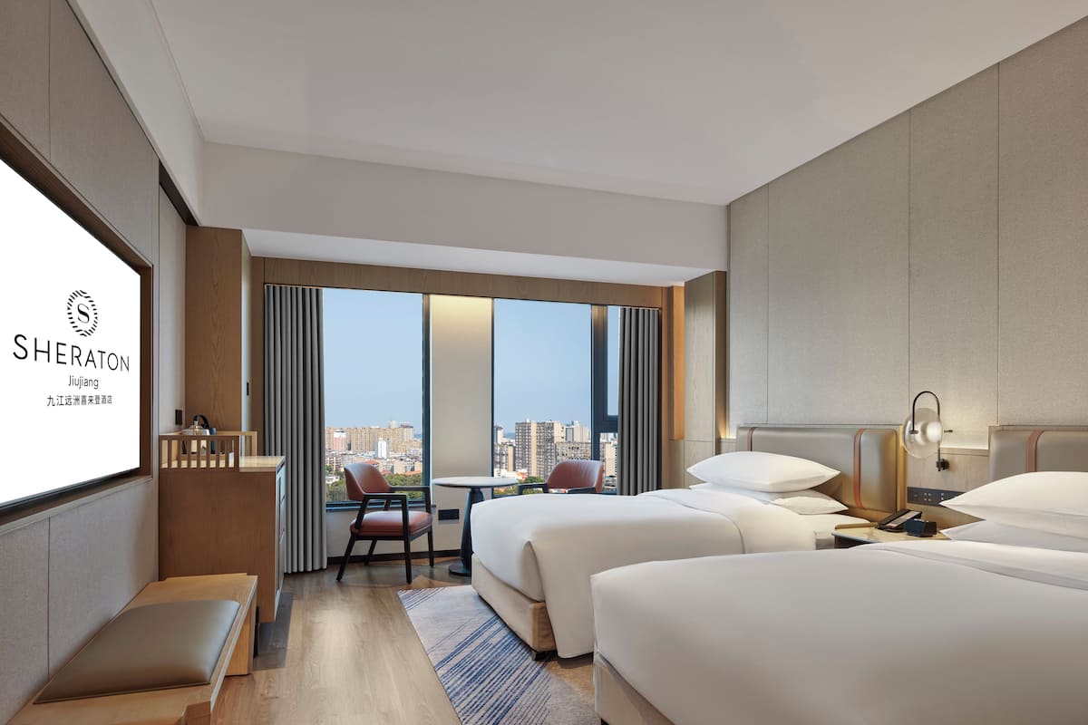 A Sheraton hotel room with two beds, a desk, a chair, and a view of the city.