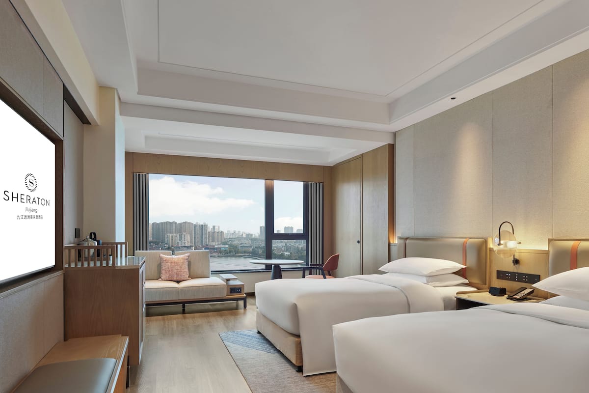 A hotel room with a large window, two beds, a desk, and a seating area.