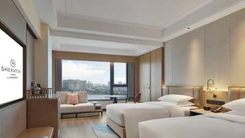 A hotel room with a large window, two beds, a desk, and a seating area.