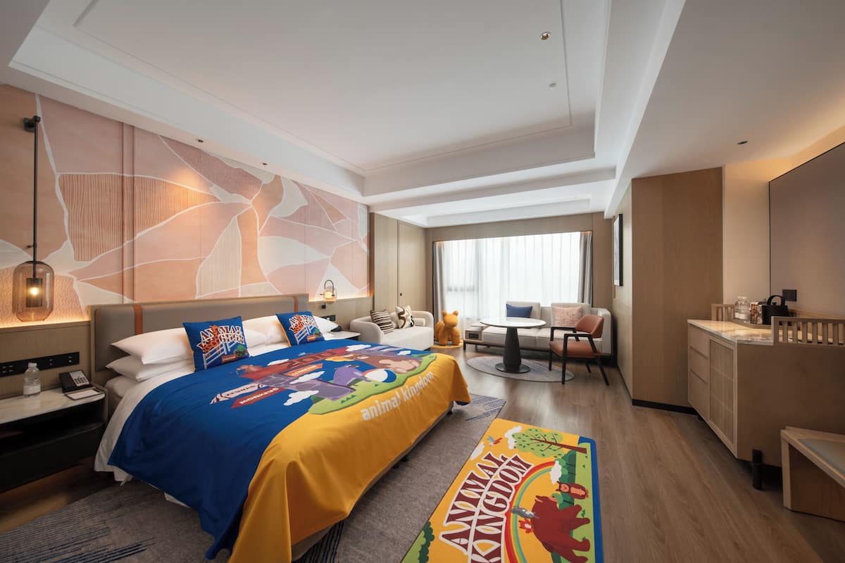 A hotel room with a large bed, a desk, a chair, a small table, and a window.