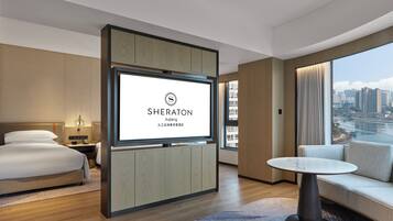 A Sheraton hotel room with a bed, bedside tables, a TV, a sofa, and a view of a cityscape.