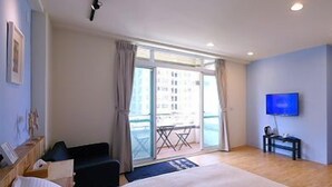 Ein Hotelzimmer mit einem großen Bett, einem Fernseher, einem Balkon mit Tisch und Stühlen und Blick auf Gebäude.