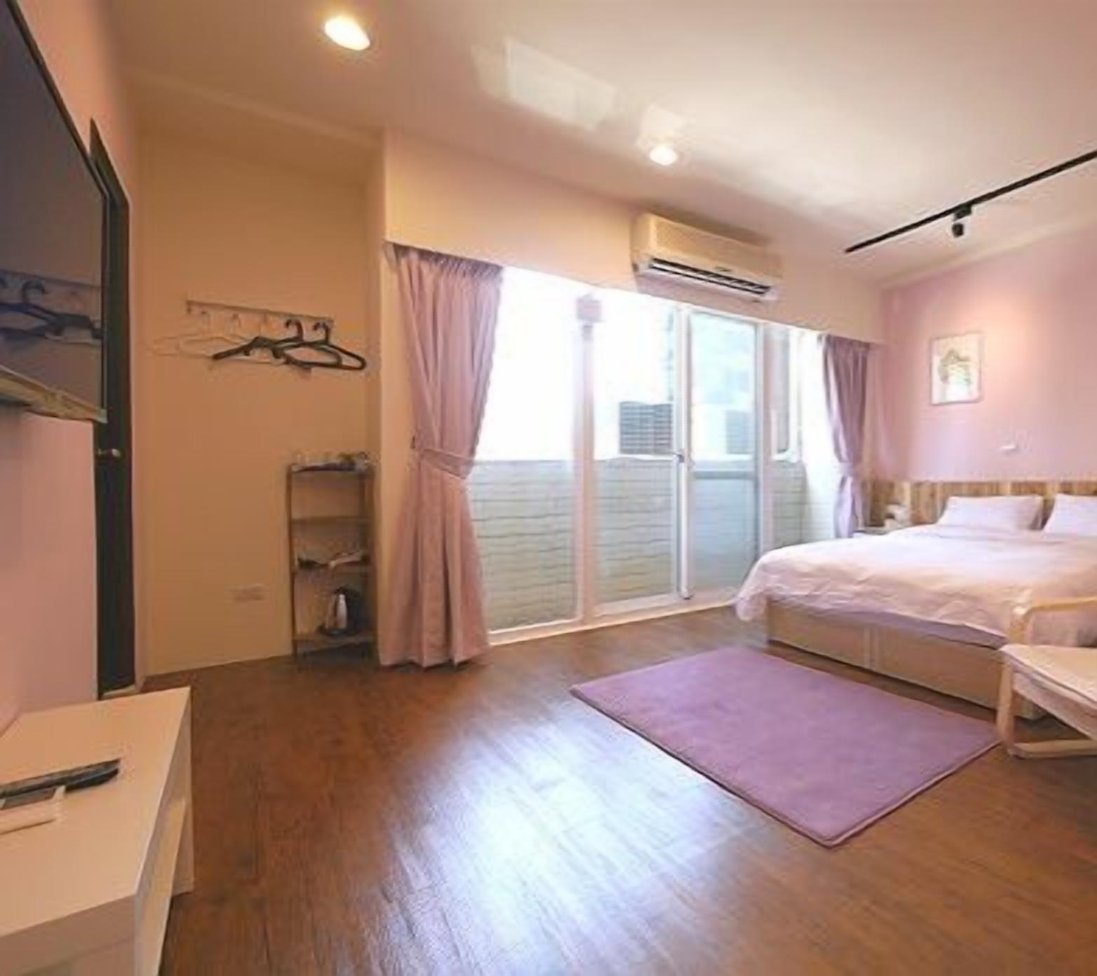 A bedroom with a bed, a bedside table, a hanging light, a window with curtains, and a sliding door to the outside.