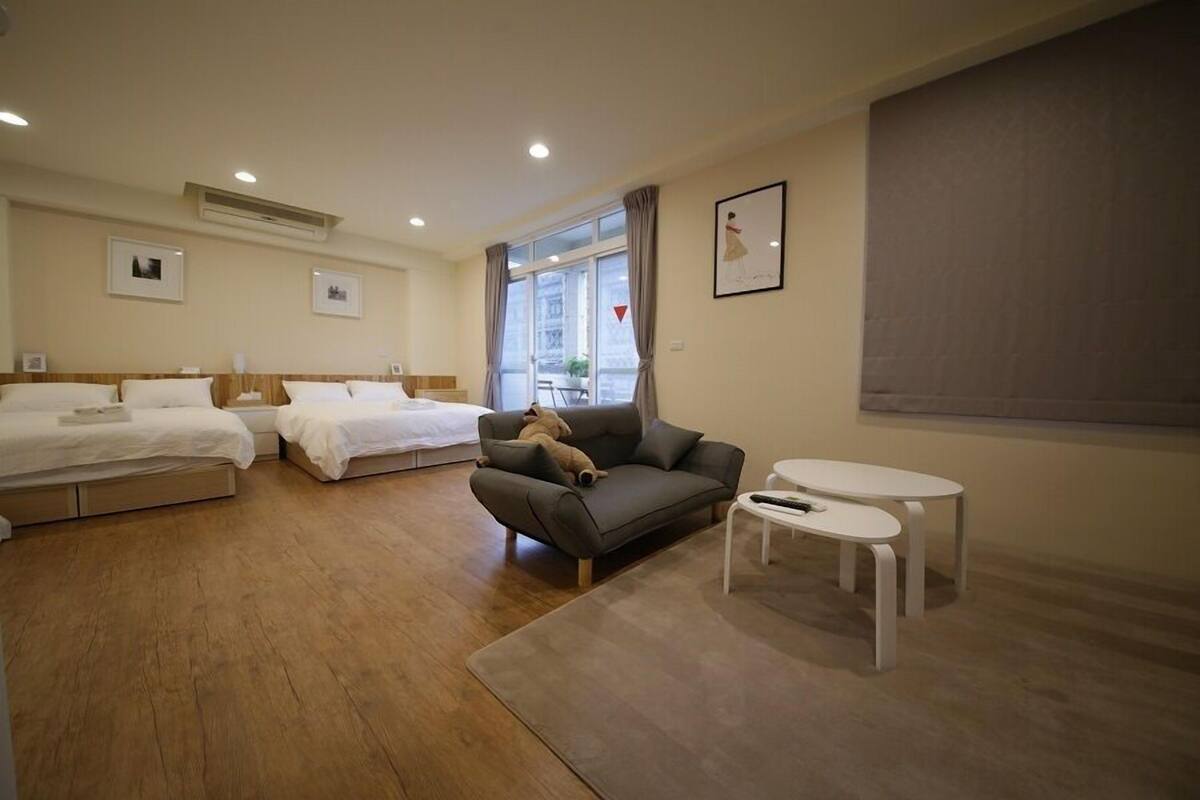 A hotel room with two single beds, a sofa, a small table, and a window with curtains.