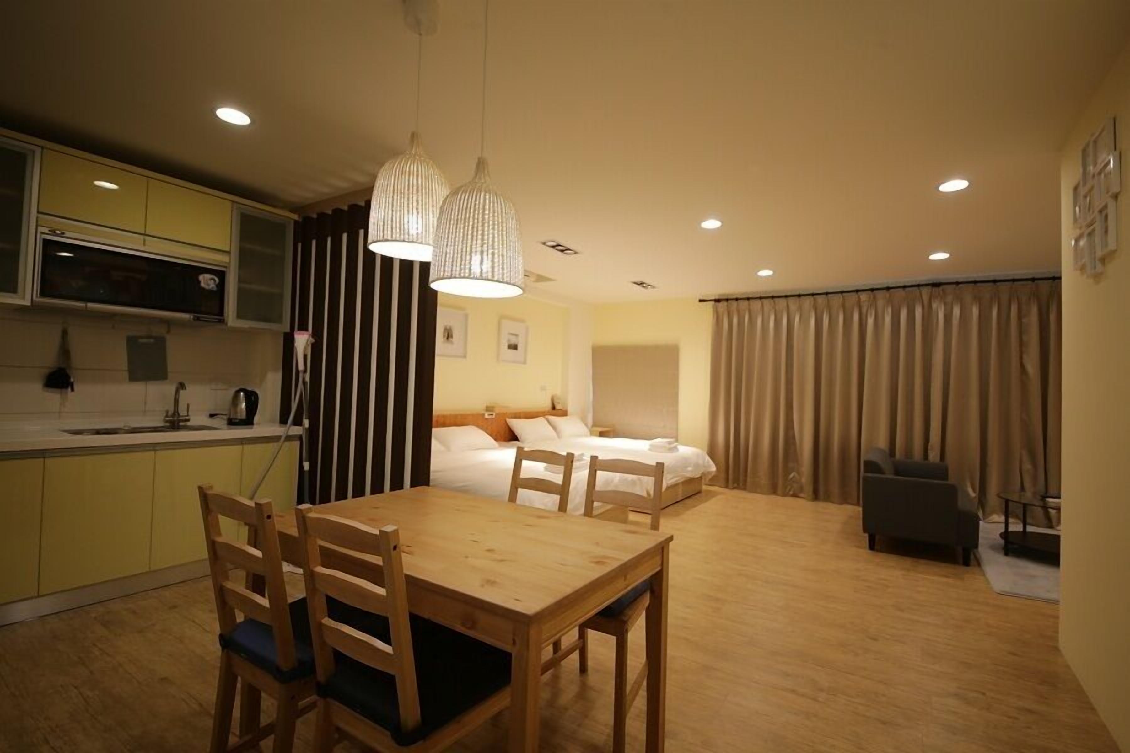 A compact hotel room with a dining area, a kitchenette, and a bed with a headboard.