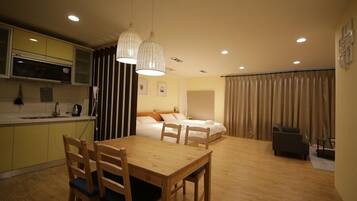 A compact hotel room with a dining area, a kitchenette, and a bed with a headboard.