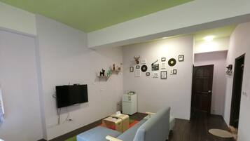 A compact living space with a sofa, a television, a small table, and a refrigerator.
